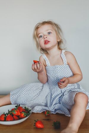 cute European girl eating strawberries. a beautiful, cheerful blonde with blue eyes.の写真素材