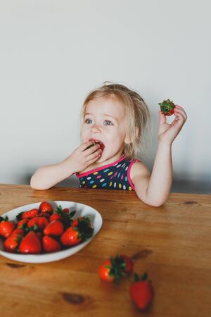 cute European girl eating strawberries. a beautiful, cheerful blonde with blue eyes.の写真素材