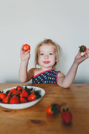 cute European girl eating strawberries. a beautiful, cheerful blonde with blue eyes.の写真素材