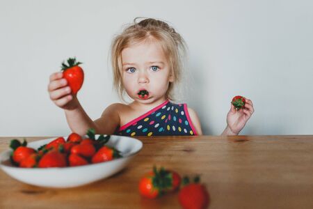 cute European girl eating strawberries. a beautiful, cheerful blonde with blue eyes.の写真素材