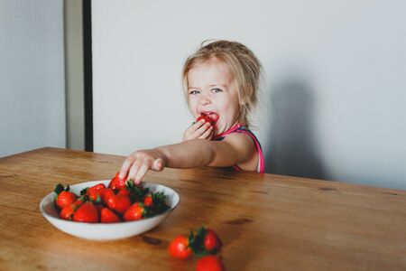 cute European girl eating strawberries. a beautiful, cheerful blonde with blue eyes.の写真素材