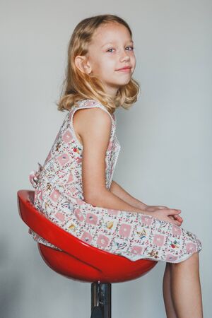 sweet European teen girl on a gray background sitting on a red chair. beautiful curly blonde with white teeth.の写真素材