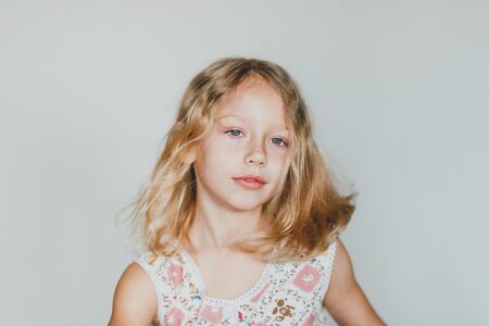 cute European teen girl on a gray background sitting on a red chair. beautiful curly blonde with white teeth. close upの写真素材