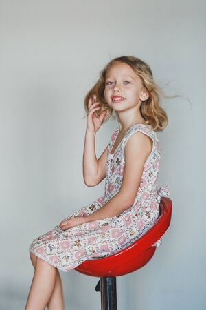 cute European teen girl on a gray background sitting on a red chair. beautiful curly blonde with white teeth.の写真素材