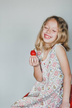 European blonde girl eating strawberries on a gray background. white teeth. useful berryの写真素材