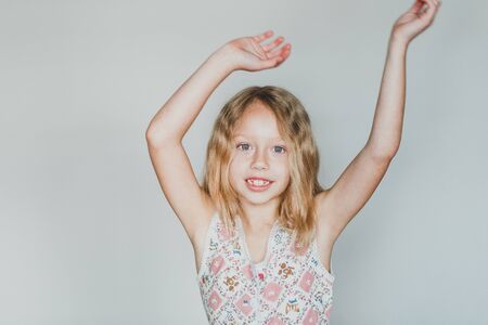 cute european teen girl on a gray background hands up. beautiful curly blonde with white teeth.の写真素材