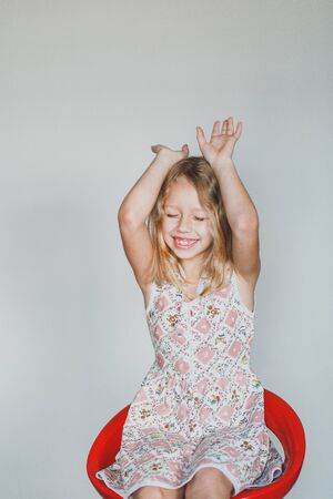 cute European teen girl on a gray background sitting on a red chair. beautiful curly blonde with white teeth. bunnyの写真素材