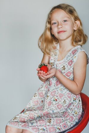 European blonde girl eating strawberries on a gray background. vitamins for childrenの写真素材
