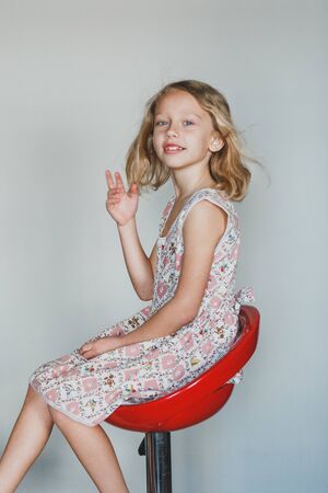 cute European teen girl on a gray background sitting on a red chair. beautiful curly blonde with white teeth. an expressive smileの写真素材