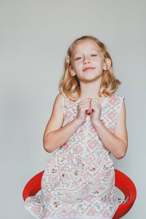 tricky European teen girl on a gray background sitting on a red chair. beautiful curly blonde with white teeth.の写真素材