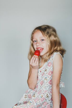 European blonde girl eating strawberries on a gray background. white teeth.の写真素材