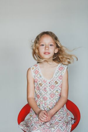 looking at the camera European teen girl on a gray background sitting on a red chair. beautiful curly blonde with white teeth.の写真素材