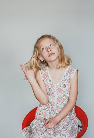 cute European teen girl on a gray background sitting on a red chair. beautiful curly blonde with white teeth. musedの写真素材
