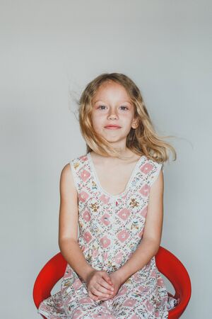 looking at the camera European teen girl on a gray background sitting on a red chair. beautiful curly blonde with white teeth.の写真素材