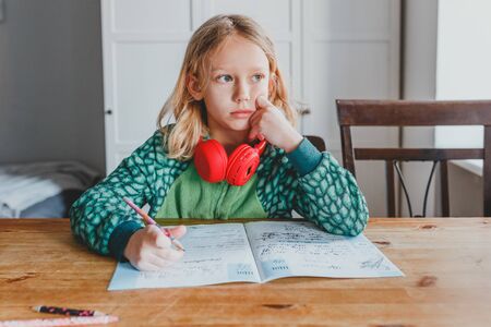 European blonde girl sitting and doing homework. the schoolgirl thought about it.の写真素材