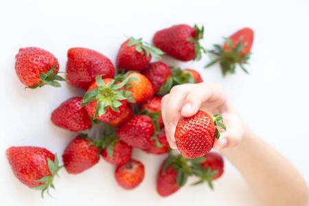 juicy strawberry lies on a white background. the view from the top. a childs hand takes a berryの写真素材