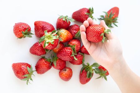 juicy strawberry lies on a white background. the view from the top. a childs hand takes a berryの写真素材