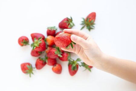 juicy strawberry lies on a white background. the view from the top. a childs hand takes a berryの写真素材