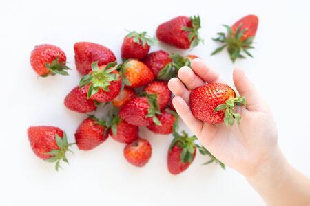 juicy strawberry lies on a white background. the view from the top. a childs hand takes a berryの写真素材