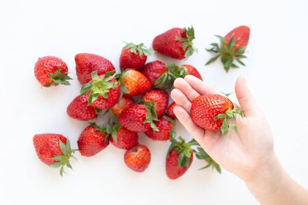 juicy strawberry lies on a white background. the view from the top. a childs hand takes a berryの写真素材
