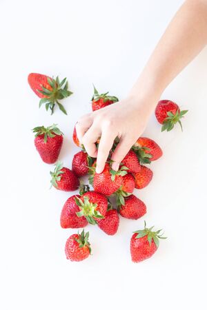 juicy strawberry lies on a white background. the view from the top. a childs hand takes a berryの写真素材