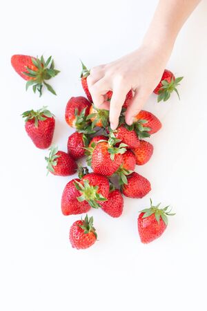 juicy strawberry lies on a white background. the view from the top. a childs hand takes a berryの写真素材