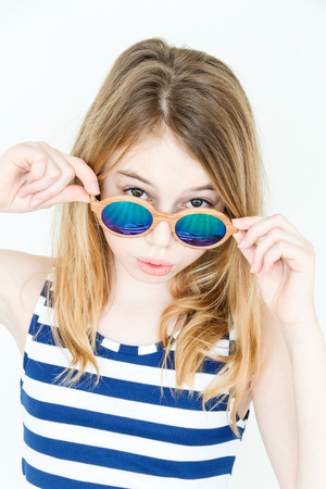 Cute blond girl eleven years old standing near white wall with green sunglassesの写真素材