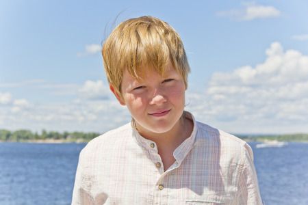 Portrait of squint blond boy in a white shirt near riverの写真素材