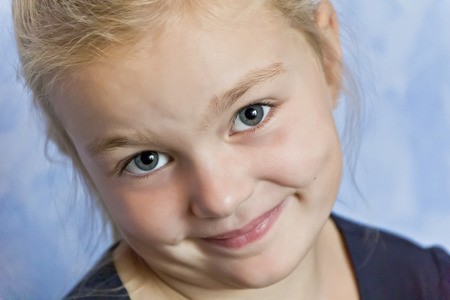 Cute smiling girl with blond hair on blue backgroundの写真素材
