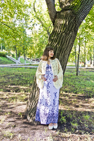 Pregnant woman with brown hair near tree in parkの写真素材