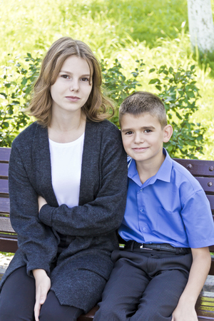 Brother and sister are sitting on bench in summerの写真素材