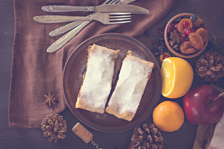 Apple strudel (pie) with dried fruits, oranges, cranberries, walnuts with sugar  on dark background.   Lunch, dinner for two. Romantic dinner.の写真素材
