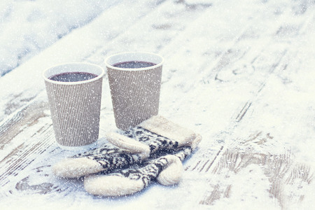 Two paper craft glass,  cup  with a hot drink, coffee, cocoa, mulled wine and white and black mittens on the table outdoor in the winter. Winter time concept. Bask in the cold.の写真素材
