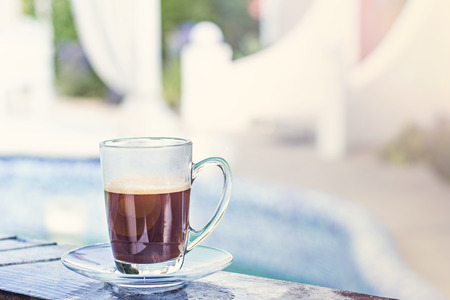 A cup of espresso and a pool and a white building in the background. Morning coffee. Summer Breakfast. Coffee at the resort.の写真素材