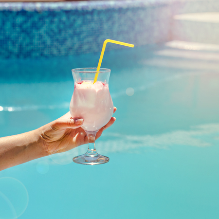 Summer cocktail in a woman's hand on the background of the pool. Pina colada, milk cocktail, berry cocktail. Summer vacation, relaxation, summer party.の写真素材