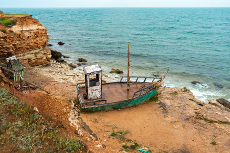 An old rusty abandoned boat is located on the seashore. Rocks and blue sea in the background.の写真素材