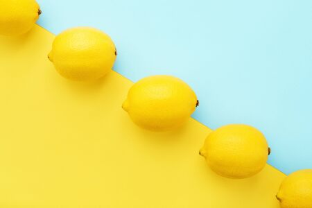 Lemons in row on pastel yellow and blue background. Minimal style, summer concept. Flat lay, absrtact, trendy pattern.の写真素材