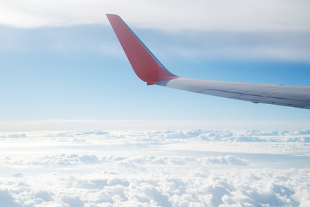 Aerial view from airplane window on clouds and a plane wing in blue sky. Flying and traveling...