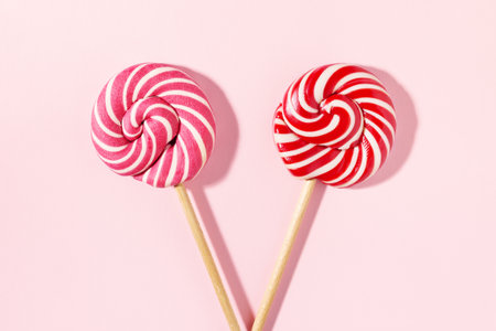Two Lollipop candy with red, white spiral stripes on pink background. Birthday concept. Flat lay, minimal.の写真素材