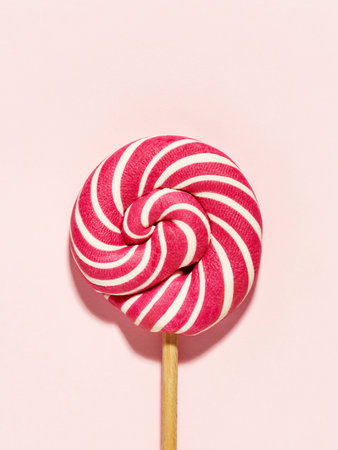 Swirly red and white Lollipop candy on pink background. Flat lay, minimal. Birthday concept.