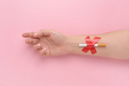 A cigarette glued with a cross to a womans hand, quit smoking concept.