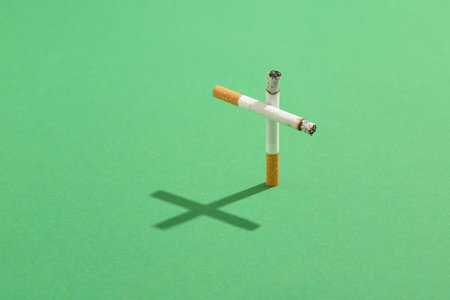 Smoking kills concept with cigarettes as a grave cross with the cross shadow on green cemetery lawn.