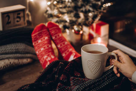 Feet in Christmas socks. Close up on feet. Winter and Christmas holidays concept. The cup of hot drink. Cozy scene. Background with christmas decor. Christmas background.の写真素材