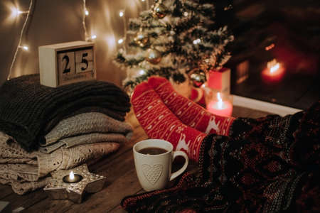 Feet in Christmas socks. Close up on feet. Winter and Christmas holidays concept. The cup of hot drink. Cozy scene. Background with christmas decor. Christmas background.の写真素材