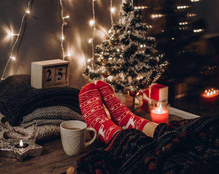 Feet in Christmas socks. Close up on feet. Winter and Christmas holidays concept. The cup of hot drink. Cozy scene. Background with christmas decor. Christmas background.の写真素材