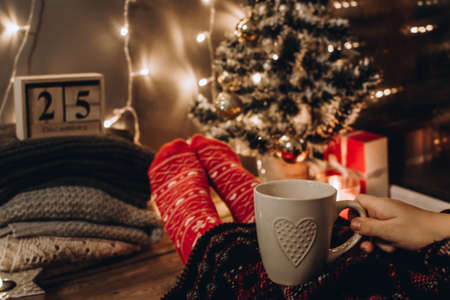 Feet in Christmas socks. Close up on feet. Winter and Christmas holidays concept. The cup of hot drink. Cozy scene. Background with christmas decor. Christmas background.の写真素材