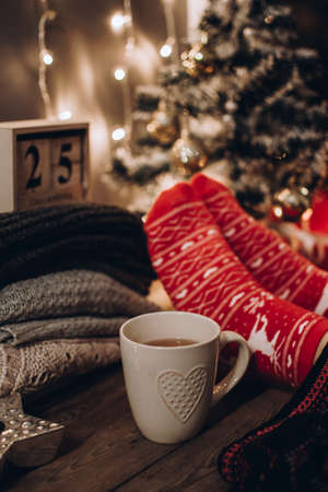 Feet in Christmas socks. Close up on feet. Winter and Christmas holidays concept. The cup of hot drink. Cozy scene. Background with christmas decor. Christmas background.の写真素材