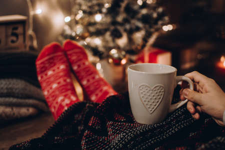 Feet in Christmas socks. Close up on feet. Winter and Christmas holidays concept. The cup of hot drink. Cozy scene. Background with christmas decor. Christmas background.の写真素材