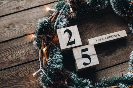 Wooden calendar blocks against a rustic wood background with Christmas wreath and lights. Background with christmas decor. Christmas background. Winter months. 25 of December.の写真素材