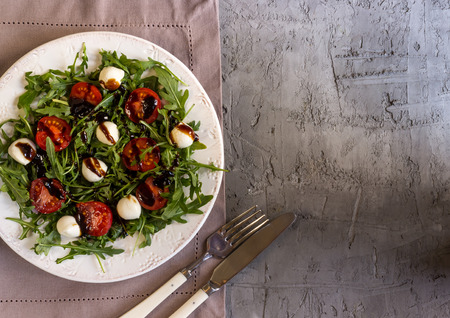 Fresh salad with arugula, mozzarella, cherry tomatoes and balsamic on a white round plate on a grey concrete background. Healthy eating concept. Top viewの写真素材